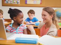 Cute pupil using computer with teacher