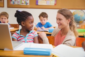 Female teacher interacts with elementary-aged girl in class.