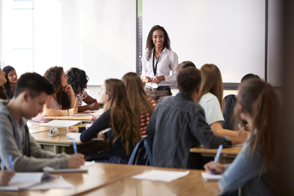 female high school teacher standing in front of interactive whiteboard teaching lesson